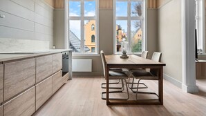 A modern kitchen with a wooden table and chairs, large windows, and a view of buildings outside. - Experience the luxury lifestyle 100m from Bryggen! (Bergenhus)