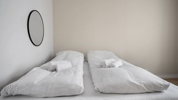Habitación minimalista con dos camas individuales, cada una con una toalla enrollada.