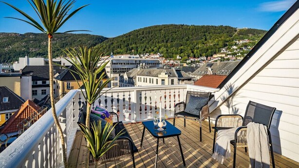 A balcony with a table and chairs, overlooking a town with buildings and hills in the background.