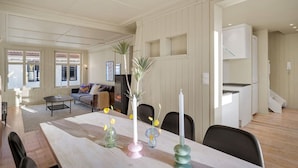 A spacious living area with a large wooden table, a sofa, and a fireplace. There are several vases with flowers on the table.