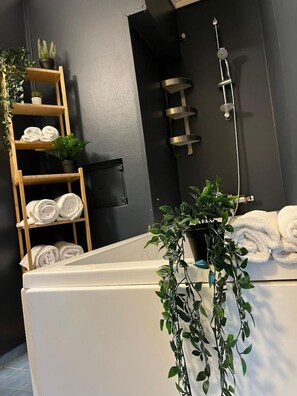 A modern bathroom with a bathtub, a wooden shelf with towels, and a potted plant.