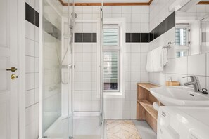 A modern bathroom with a glass shower enclosure, white tiles, a wooden vanity, and a large mirror.