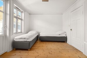 A room with two beds, wooden flooring, white walls, and a door. - Bryggen  Historical Townhouse I Rooftop Views! (Bergenhus)