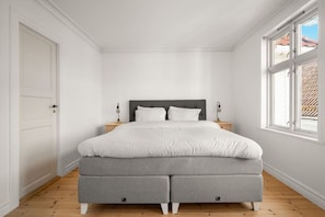 Quarto com cama, mesas de cabeceira e janela.