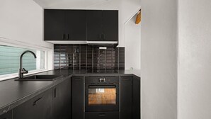 A compact kitchen with black cabinets, a stainless steel sink, and a built-in oven. - Bryggen  Historical Townhouse I Rooftop Views! (Bergenhus)