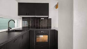 A compact kitchen with black cabinets, a stainless steel sink, and a built-in oven.