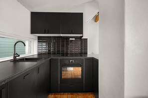 A compact kitchen with black cabinets, a stainless steel sink, and a built-in oven. - Bryggen  Historical Townhouse I Rooftop Views! (Bergenhus)