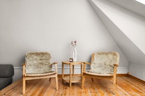 A room with two chairs with fur upholstery, a small wooden table with a vase and a candle, and a sloped ceiling. - Bryggen  Historical Townhouse I Rooftop Views! (Bergenhus)