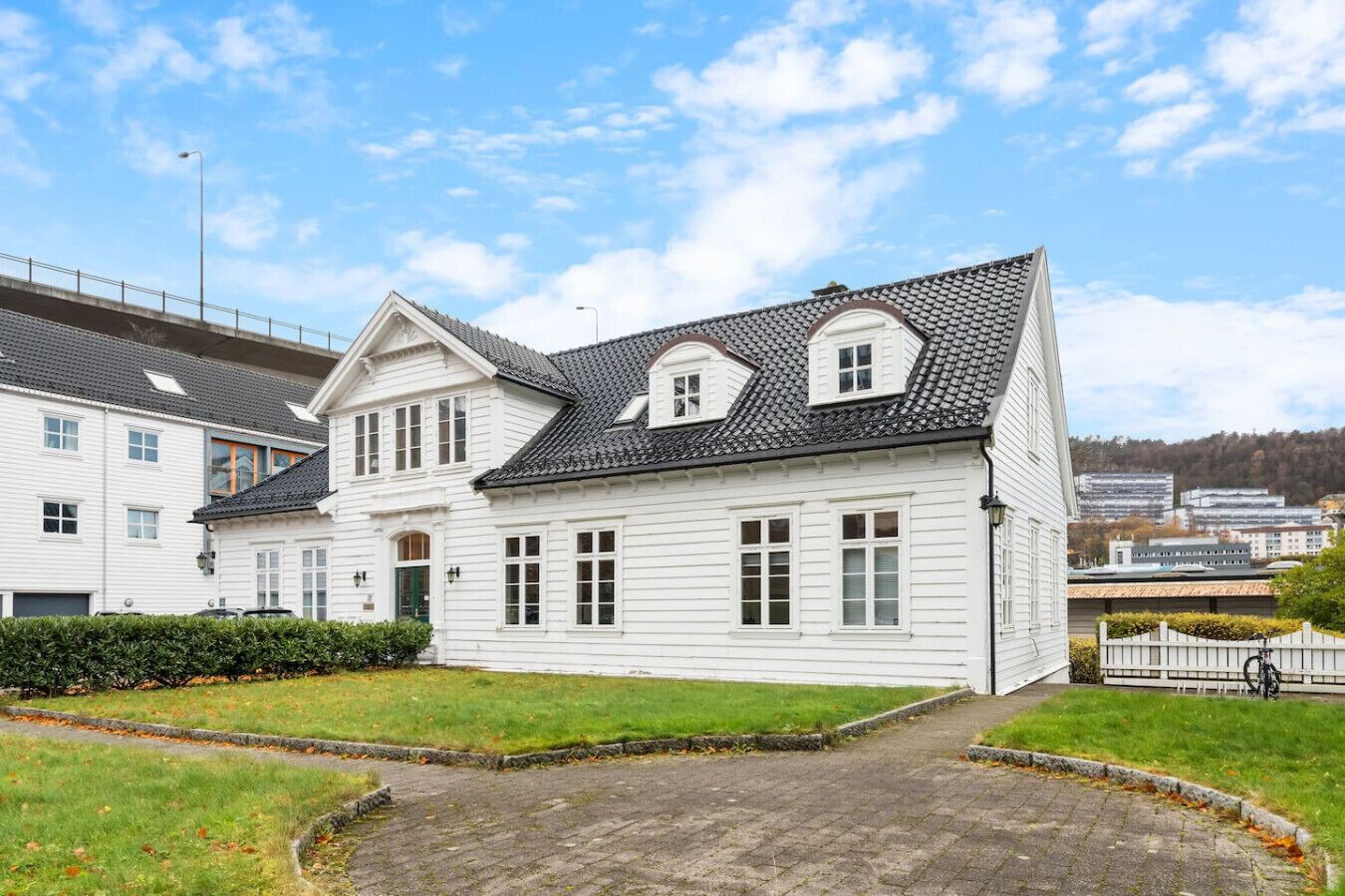 Een wit, twee verdiepingen hoog huis met pannendak, een veranda en een geplaveid oprit.