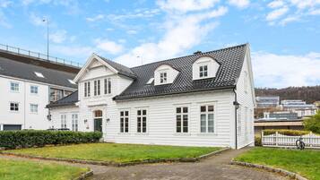 Een wit, twee verdiepingen hoog huis met pannendak, een veranda en een geplaveid oprit.