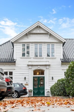 A two-story white building with a green door, parked cars, and autumn leaves on the ground.