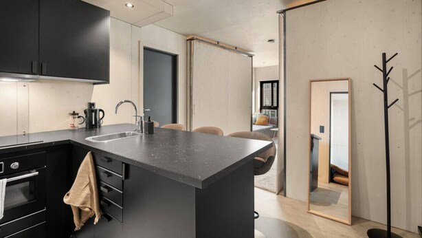 A modern kitchen with a large island, black cabinetry, and a visible coffee maker. - The Double Date I  Architectural (Bergenhus)
