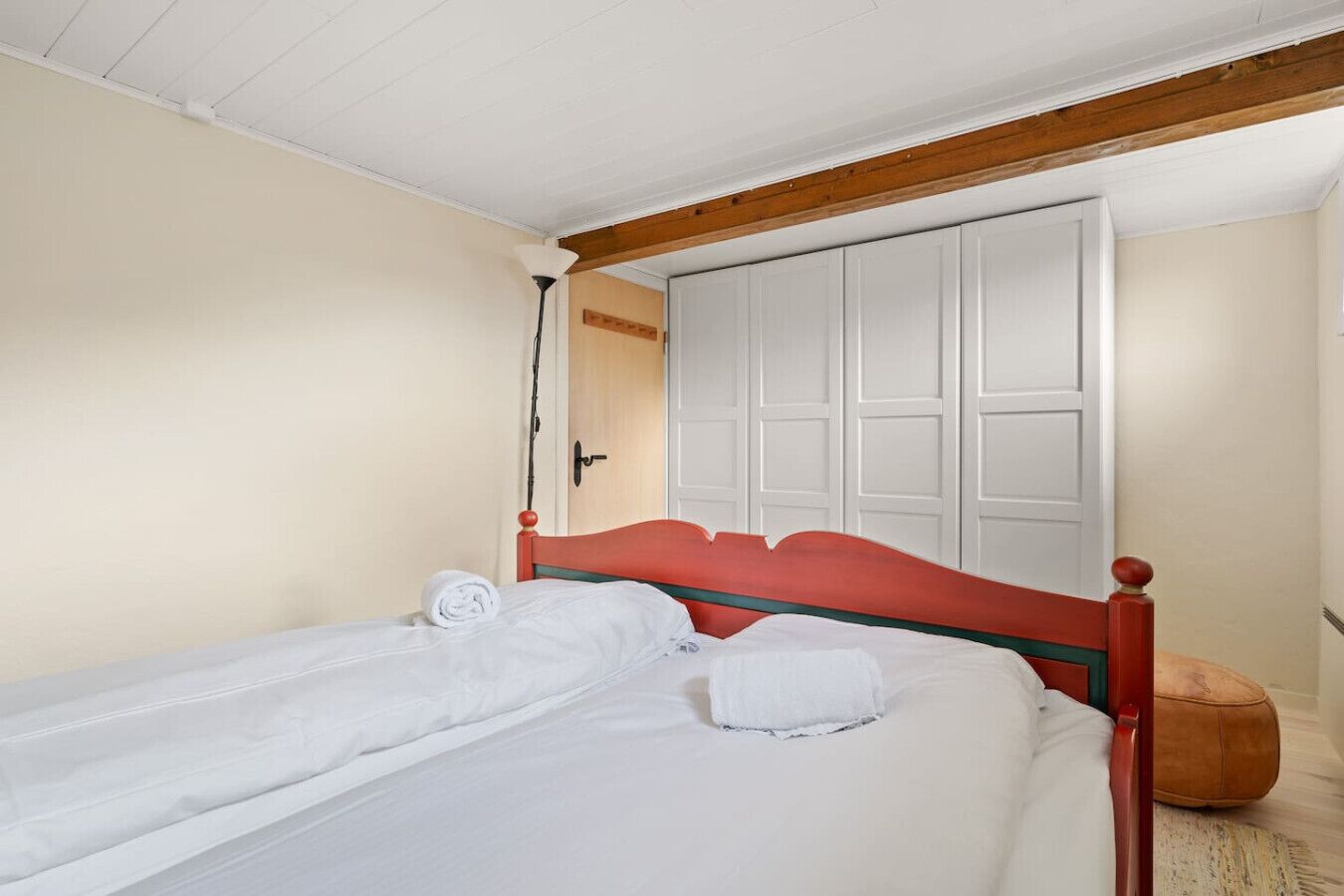 A single bed with a red headboard in a room with white walls and a wooden ceiling.