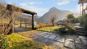 Un sentier de pierres menant à une porte rustique, entourée de verdure et avec une montagne en arrière-plan.