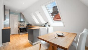 Una cocina moderna con una mesa de comedor de madera y sillas blancas, horno empotrado y vistas de la ciudad a través de tragaluces.