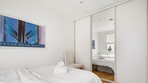 Una habitación de hotel con una cama, una silla, un espejo y un cuadro en la pared.