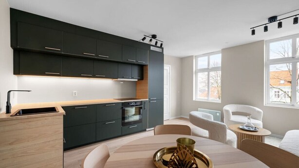 Une cuisine moderne avec des meubles de couleur sombre, un plan de travail en bois et un coin repas comprenant une table ronde et des chaises.