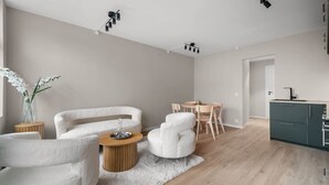 Un salon moderne comprenant un canapé, des fauteuils, une table basse et un coin repas avec une table et des chaises. Il y a également une cuisine équipée de placards et d’un évier.