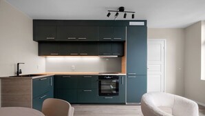 Une cuisine moderne avec des meubles de couleur sombre, un four encastré et un coin repas comprenant une table et des chaises.
