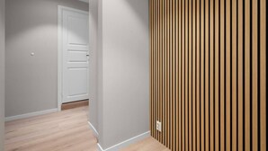 Un couloir doté d’un plancher en bois, d’une porte blanche et d’un mur recouvert de lambris en bois disposés verticalement.