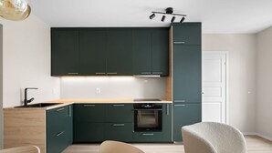 A modern kitchen with dark green cabinets, a wooden countertop, and a built-in oven. - Bergen Beds Apartments | Urban Escape (Bergenhus)