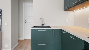 A modern kitchen with a white door, a black faucet, and teal cabinets. - Bergen Beds Apartments | Urban Escape (Bergenhus)