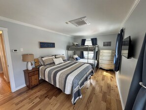 Cozy bedroom with a bunk bed, single bed, and dresser, featuring a wall-mounted TV and window with curtains.