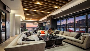 A modern living room with a large sofa set, a coffee table, and a view of a cityscape through large windows.