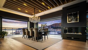 A modern dining area with a chandelier, a dining table with chairs, and a view of the sea through large windows.