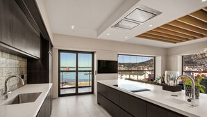 A modern kitchen with a large island, a sliding glass door to a balcony, and a view of the sea.