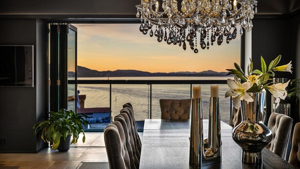 A dining area with a view of the ocean, a chandelier, and a table with candles and flowers.