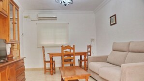 Un salon comprenant une table à manger en bois, des chaises, un canapé et un téléviseur posé sur un meuble en bois.