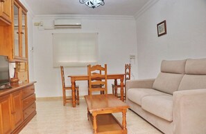 A living room with a wooden dining table, chairs, a sofa, and a TV on a wooden cabinet. - Apartamento brisa de Conil (Conil de la Frontera)