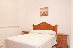 A bedroom with a wooden bed, two bedside tables, a nightstand, and a wall-mounted picture. - Apartamento brisa de Conil (Conil de la Frontera)