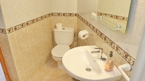 Une salle de bain comprenant des toilettes, un lavabo et une étagère en verre au-dessus du lavabo.