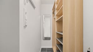 Ein schmaler Flur mit einem Holzschrank rechts, einer weißen Wand und einem schwarzen Fliesenboden.