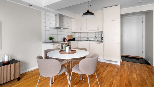 Une cuisine moderne avec des meubles blancs, une table de salle à manger ronde entourée de quatre chaises et un luminaire suspendu.