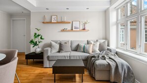 Un salon moderne avec un canapé gris, une table basse et une grande fenêtre aux cadres blancs.
