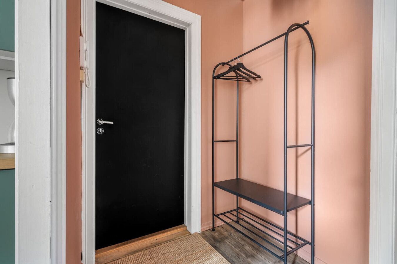 A room with a black door, a metal shelving unit with hangers, and a wooden floor.