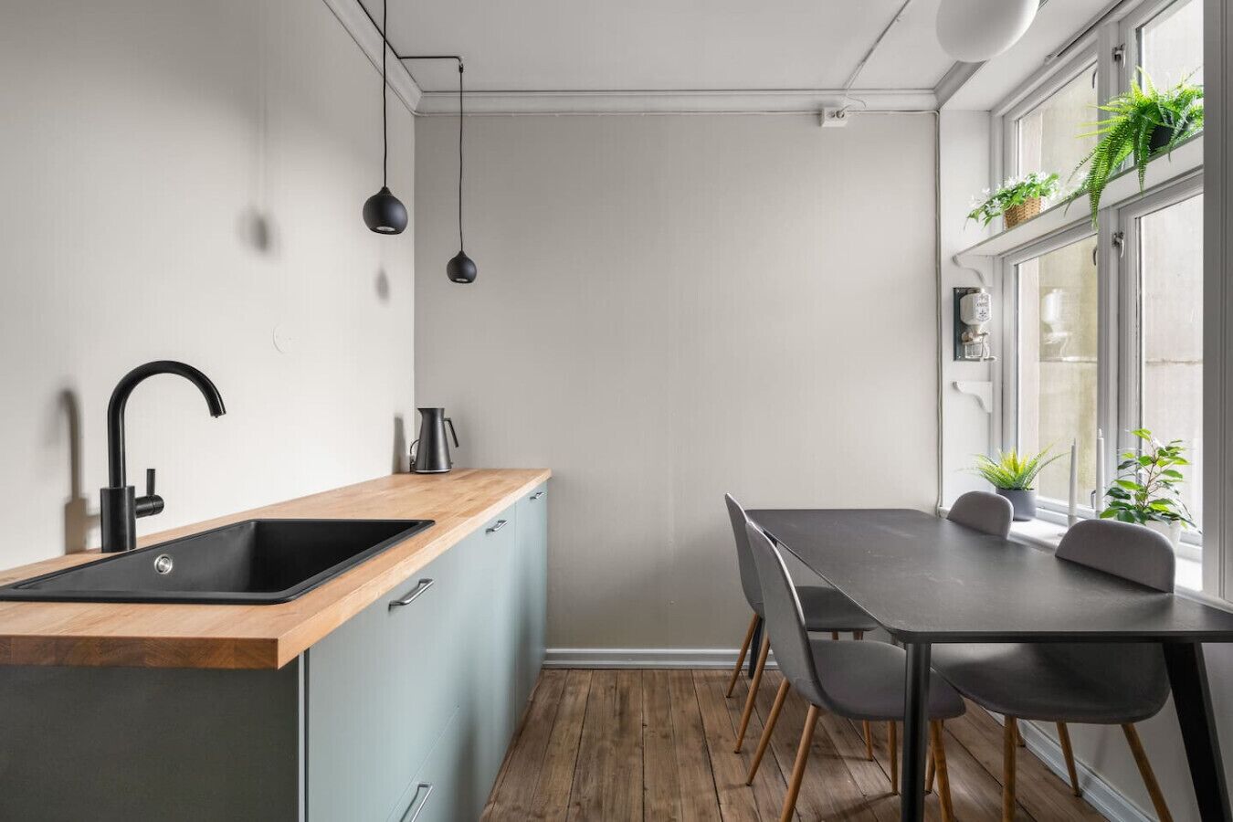 Een moderne keuken met een houten aanrechtblad, een zwarte spoelbak en een eethoek met een tafel en stoelen.