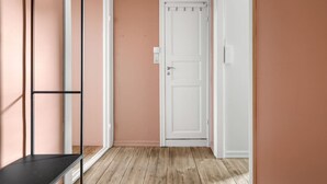 Un pasillo con una puerta blanca, un estante metálico negro y piso de madera.