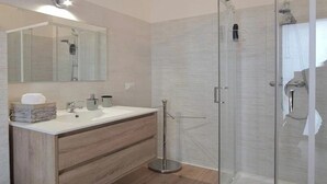 Un baño moderno con cabina de ducha de vidrio, tocador de madera con espejo y lavamanos blanco.