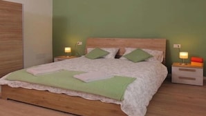 Una cama bien hecha con cabecera de madera, dos mesitas de noche con lámparas y una pared verde.