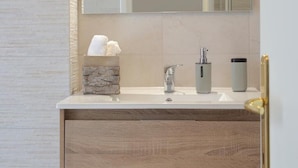 Un baño moderno con un lavamanos blanco, un detalle de piedra, un espejo y un perchero para toallas.