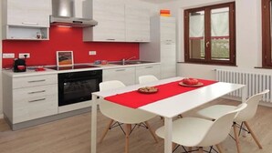 Una cocina moderna con armarios blancos, un salpicadero rojo y una zona de comedor con mesa y sillas blancas.