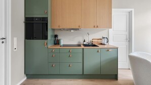 A compact kitchen with green cabinets, a wooden upper cabinet, a black oven, and a sink with a kettle.