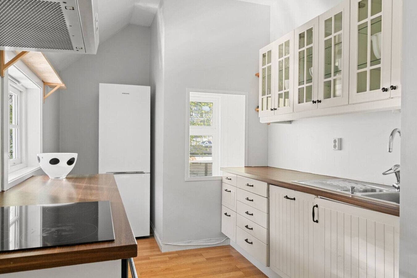 A modern kitchen with white cabinetry, a built-in oven, and a window overlooking a street.
