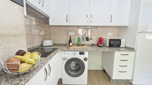 A compact kitchen with a washing machine, a toaster, a microwave, and a fruit basket.