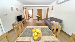 A modern living room with a dining table, a grey sofa, and a TV on a wooden stand.