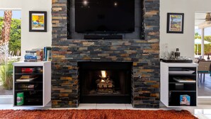 A living room with a stone fireplace, a flat-screen TV mounted above it, and a bookshelf on either side.